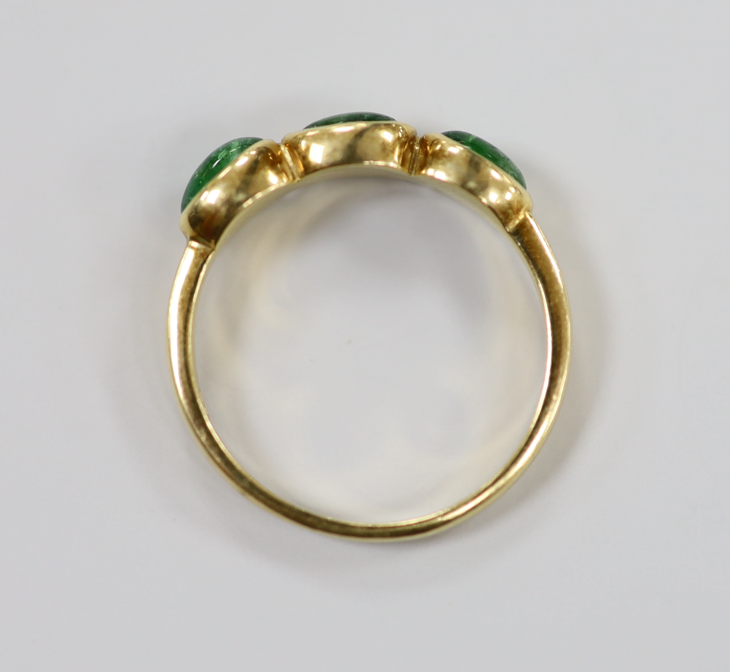 A modern 18ct gold and three stone cabochon emerald set half hoop ring, size N, gross weight 3.2 grams.